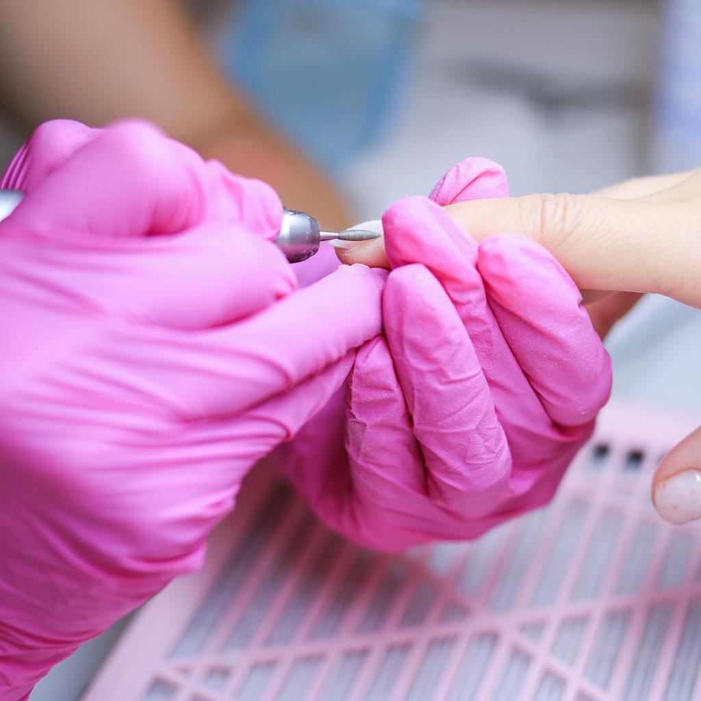 Close-up of a manicure procedure in a Polish salon with technician in pink gloves.